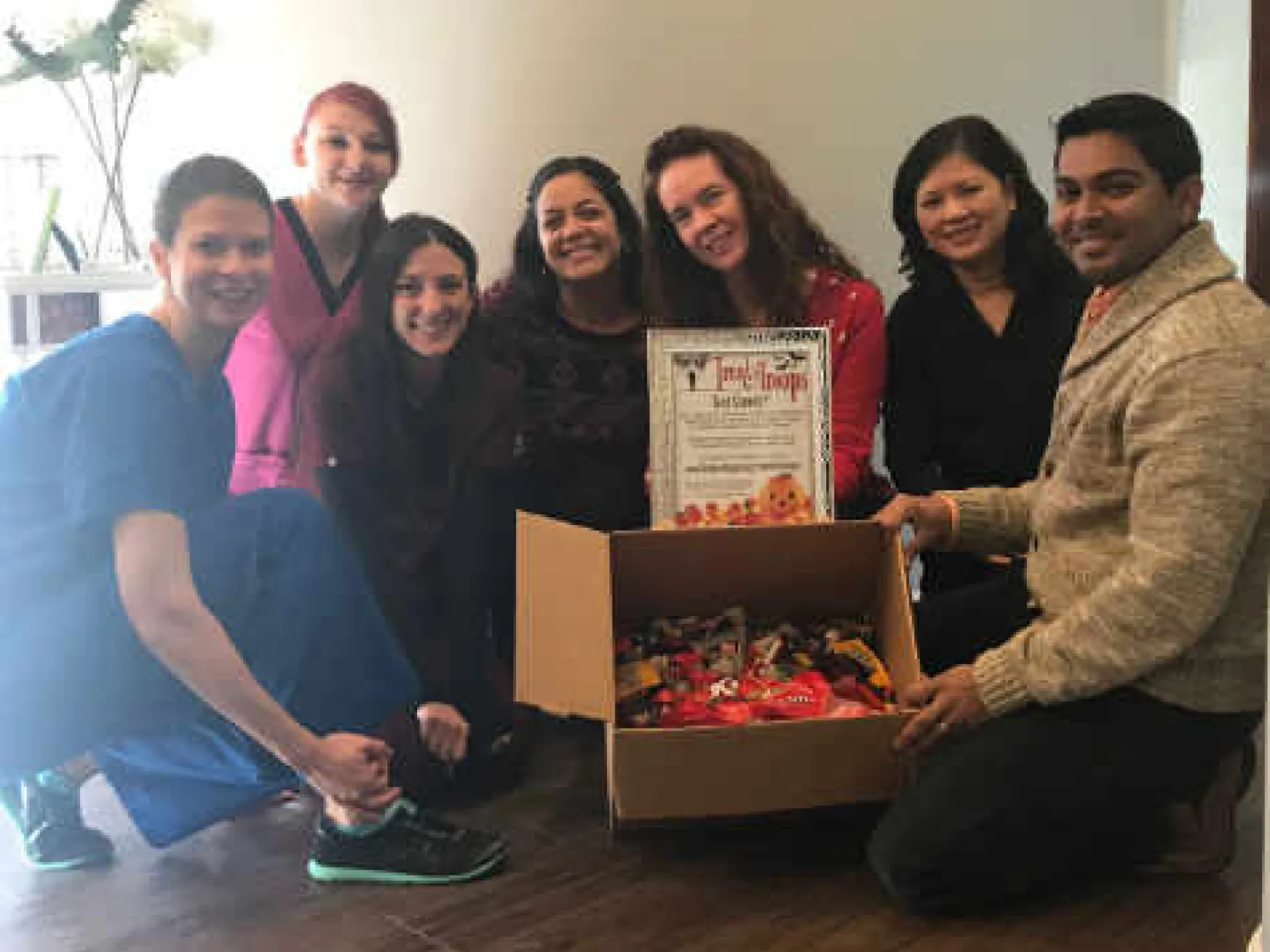 Group of seven people holding a charitable donation box and certificate in an office setting.