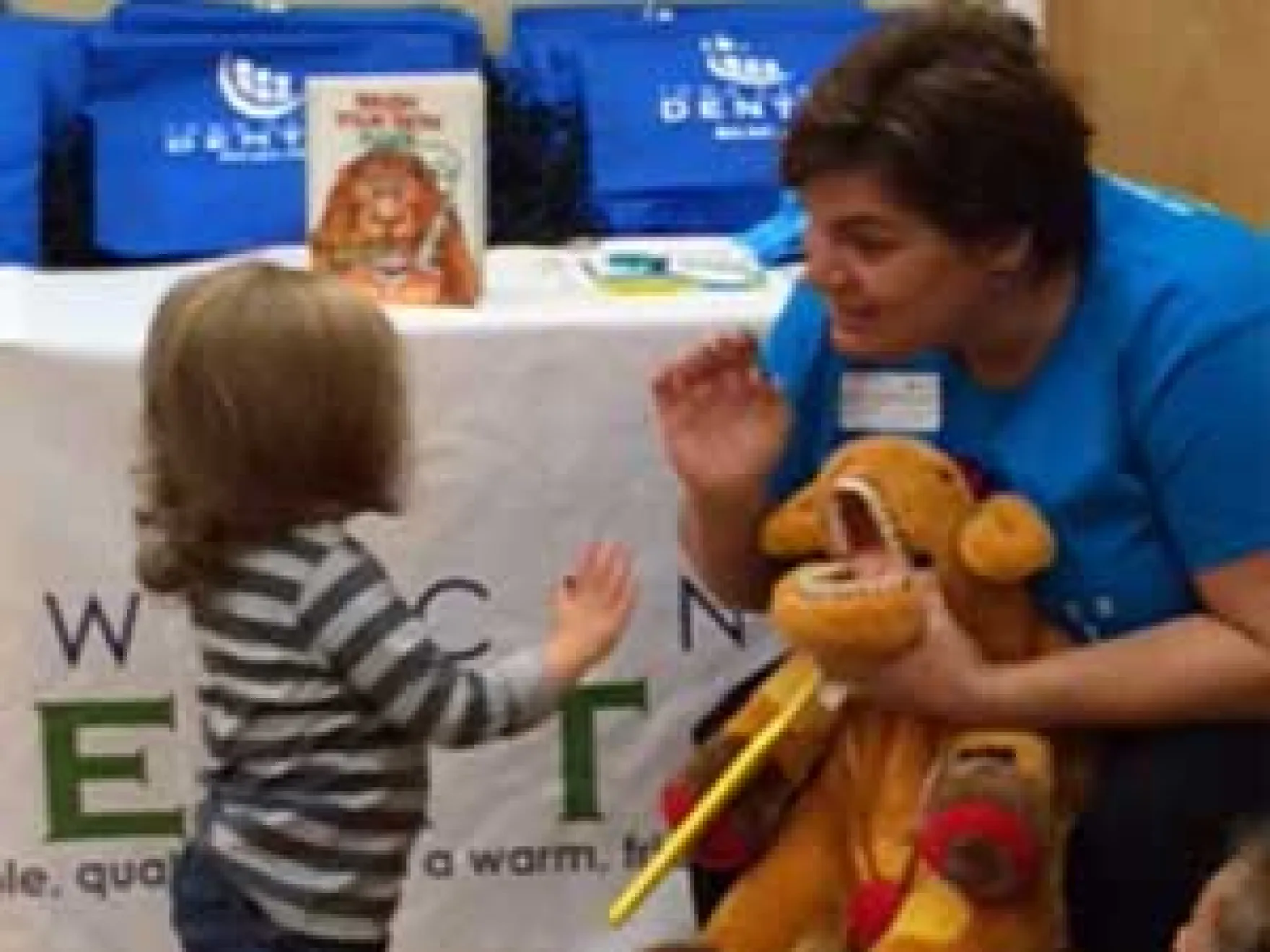Dental professional in blue shirt engages with young child during interactive educational activity at dental office event.