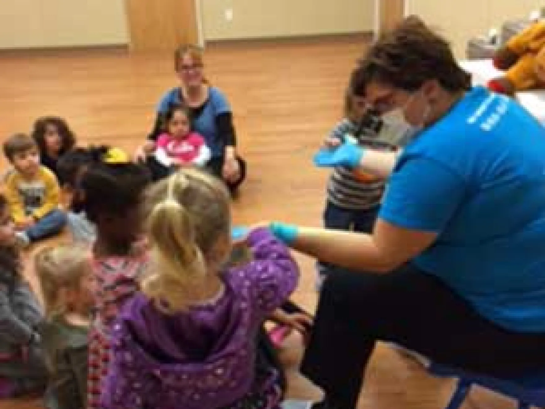 Dental professional demonstrates oral health education to group of young children in classroom setting.
