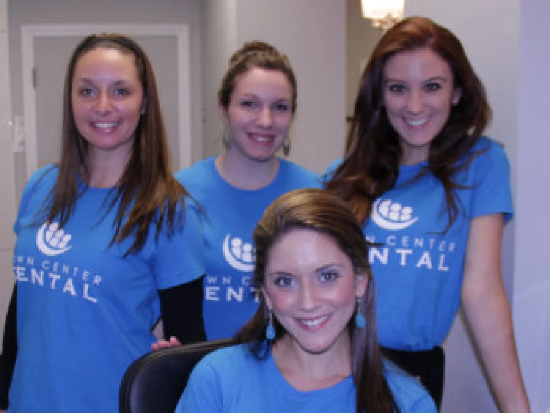 Four smiling dental staff members wearing blue Town Center Dental shirts in an indoor office setting.