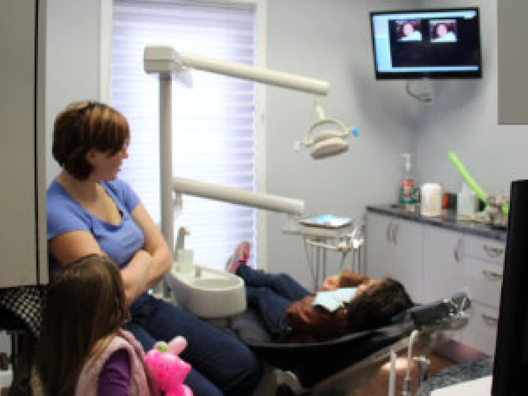 Dental hygienist assisting patient in examination chair at Town Center Dental office with overhead monitor.