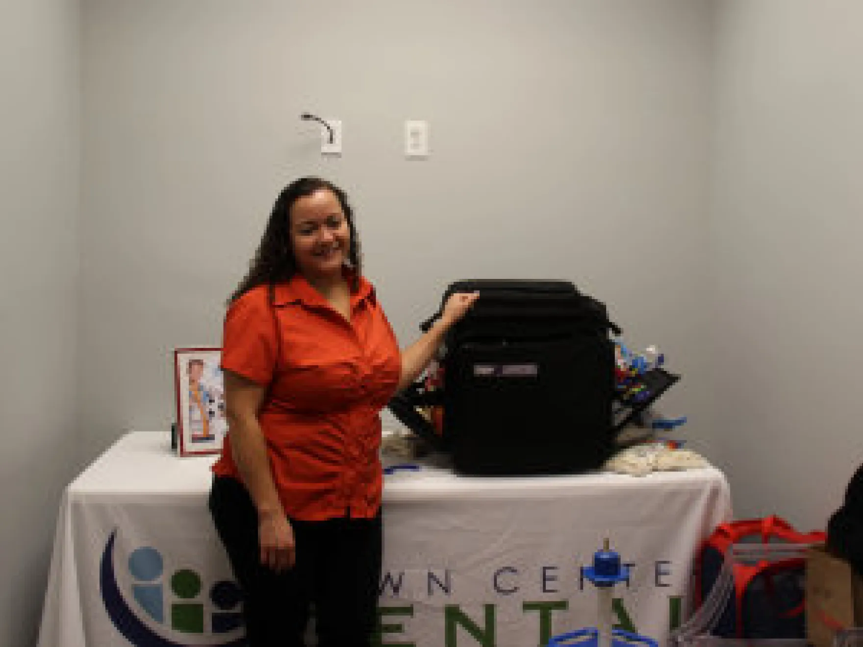 Woman in red shirt presenting backpack at Town Center Dental promotional table event.