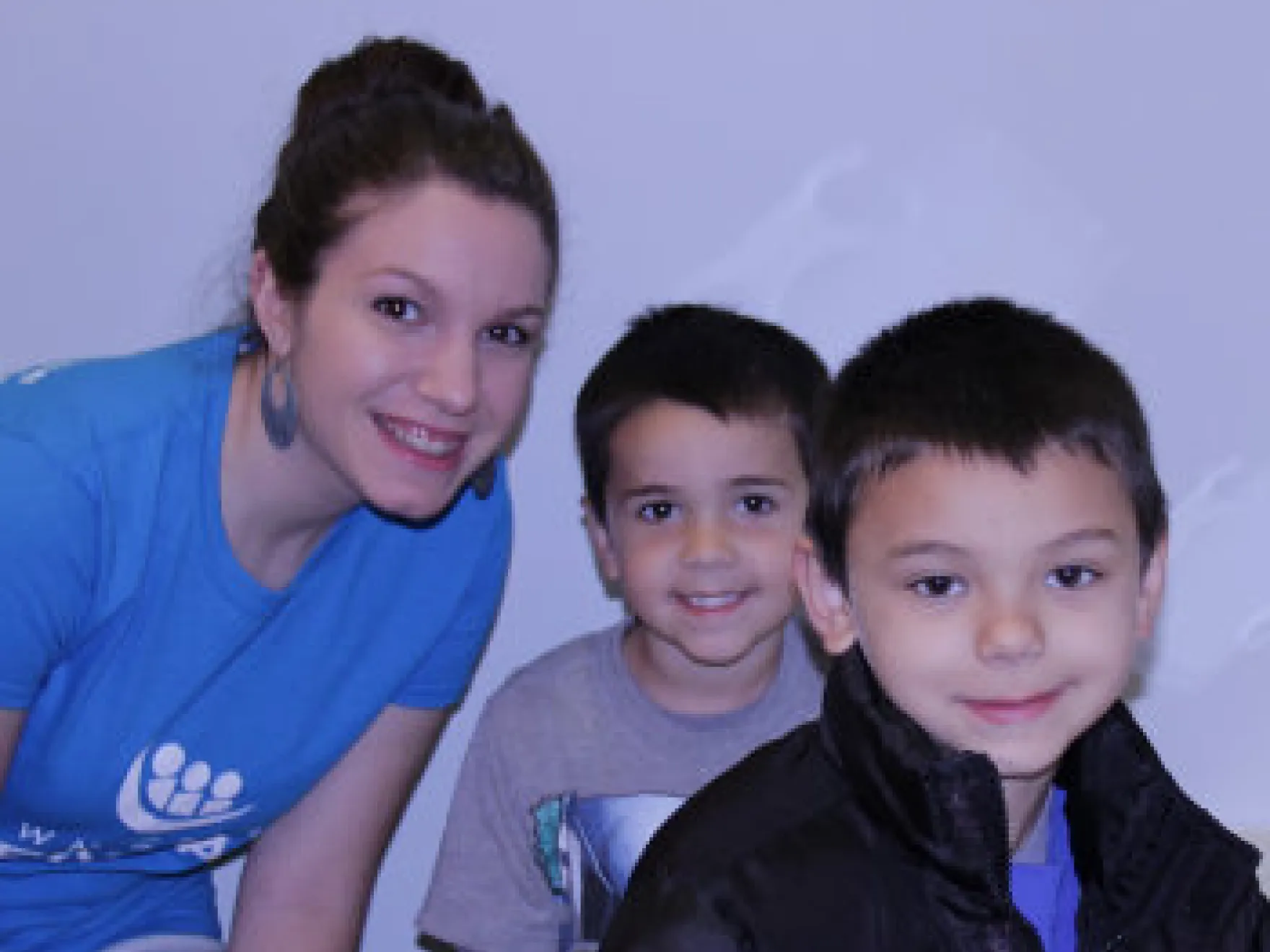 Woman and two young boys smiling at camera against blue background for dental practice portrait.