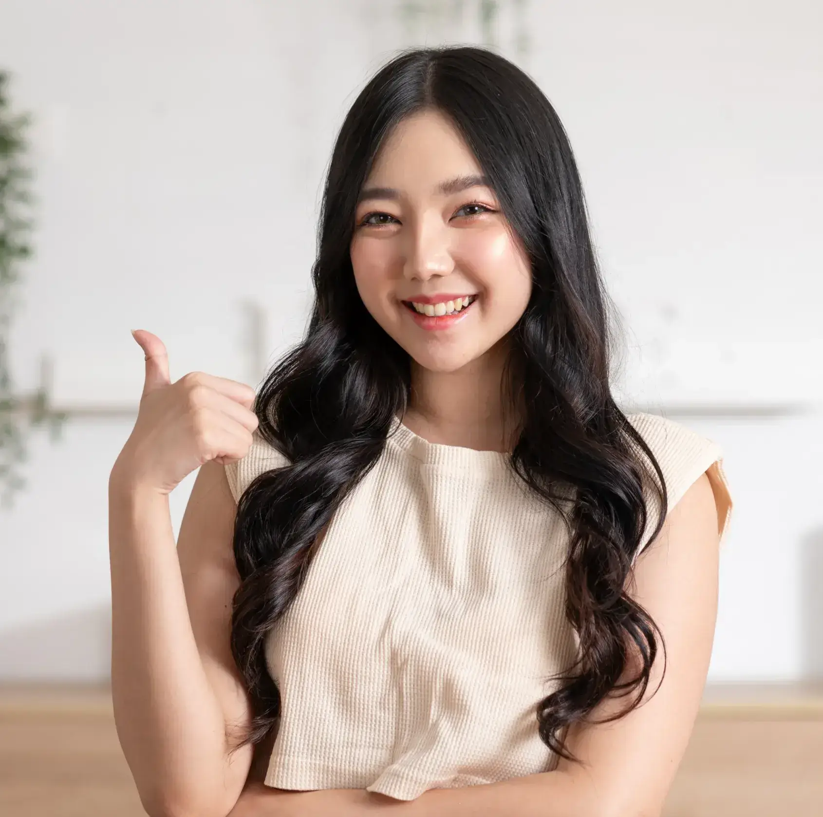 Smiling woman giving thumbs up in dental office setting, wearing beige top