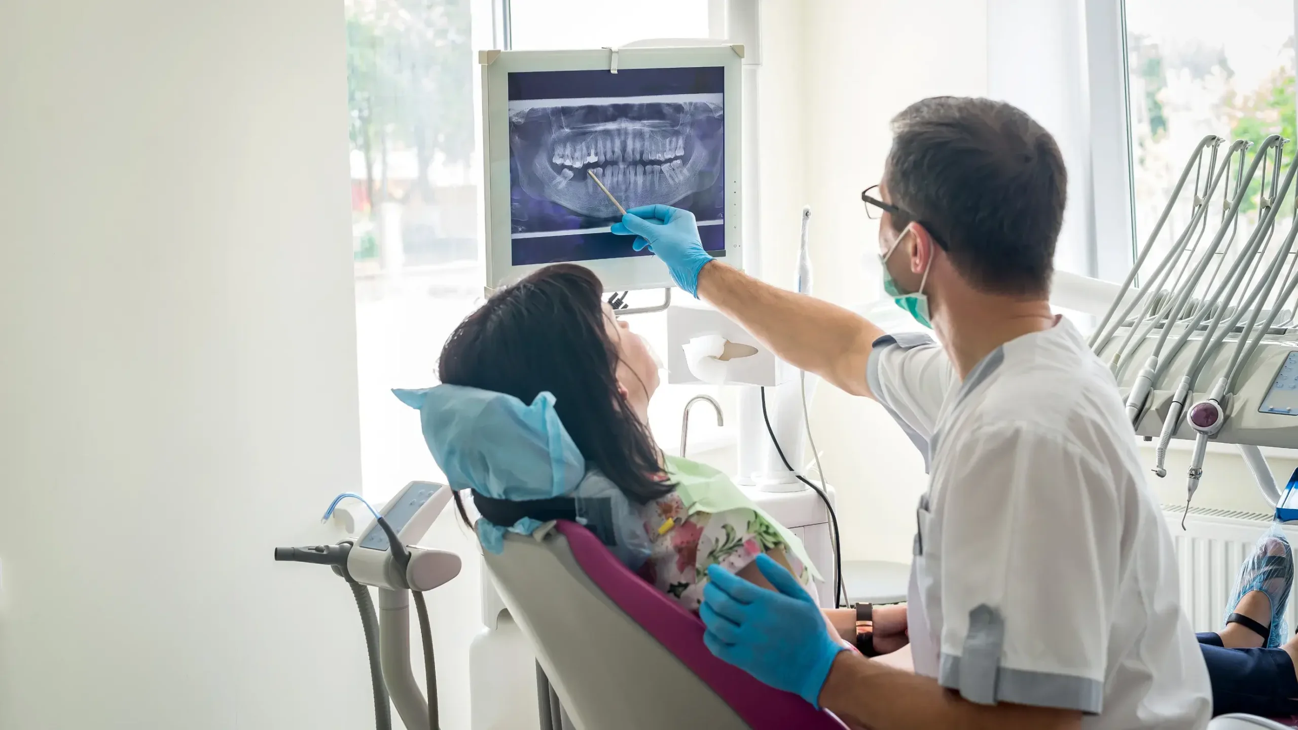 Dentist reviewing panoramic dental X-ray with patient in modern dental office examination room.