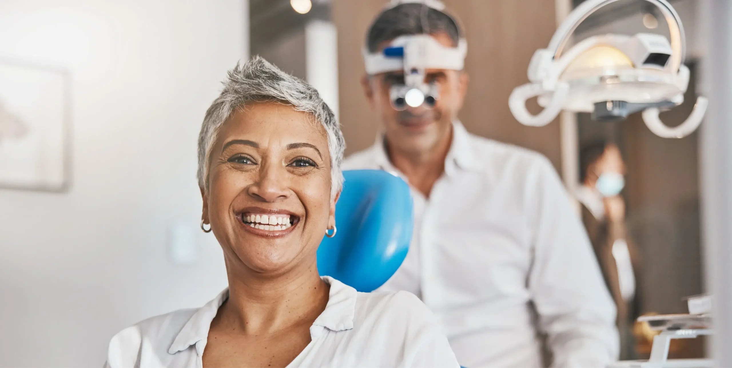 Smiling dental professional in white coat with team members in modern dental office setting.