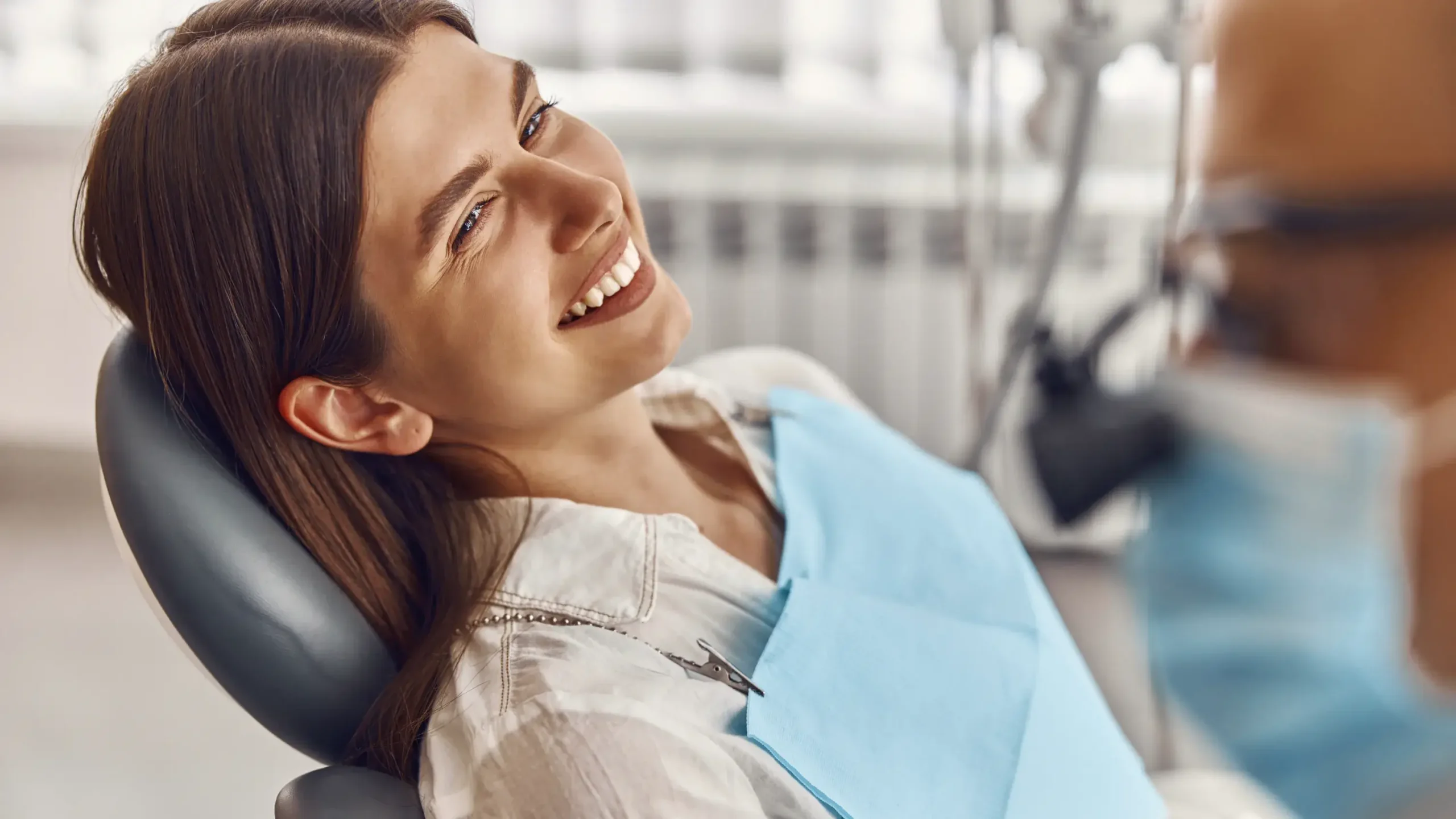 Smiling woman in dental chair during examination at dental office with dentist in background.