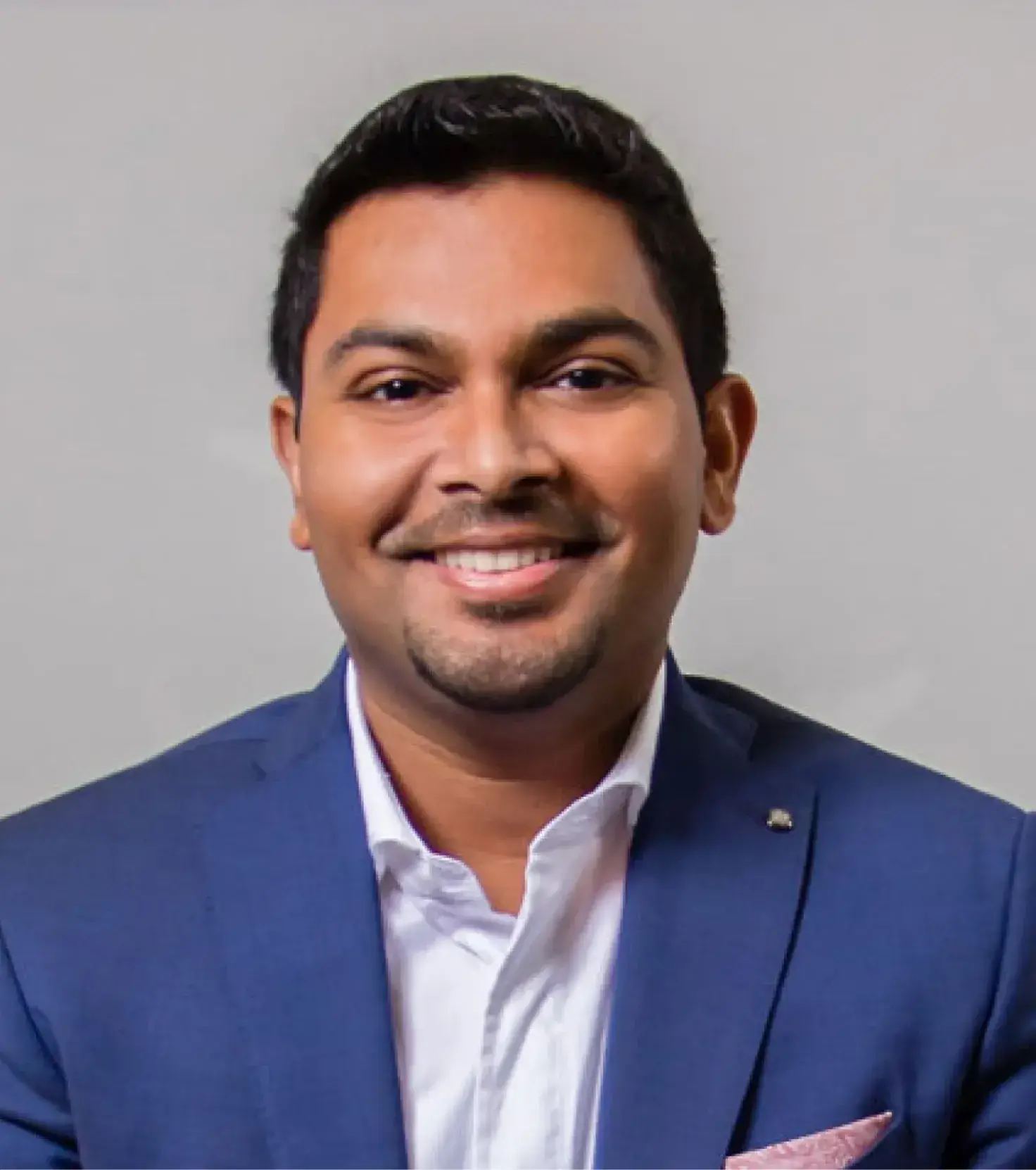 Professional headshot of smiling man in navy blazer and white shirt against gray background.