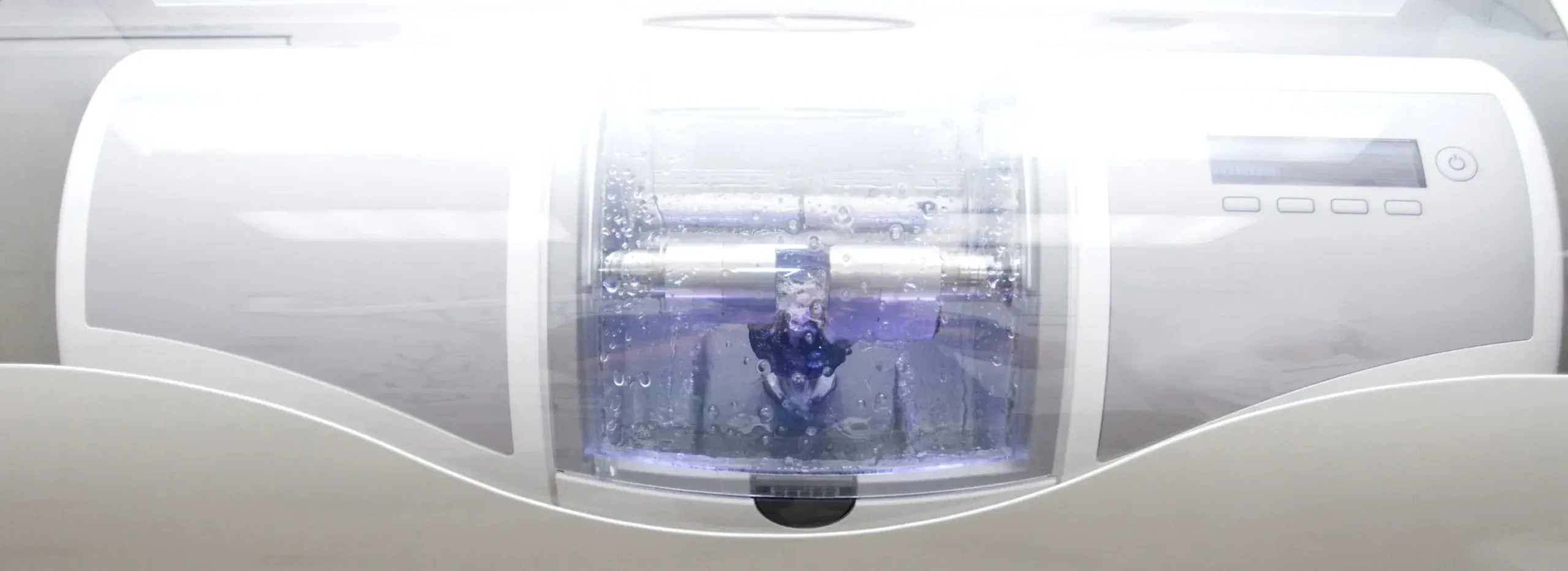Dental ultrasonic cleaner with water and instruments visible inside transparent chamber.