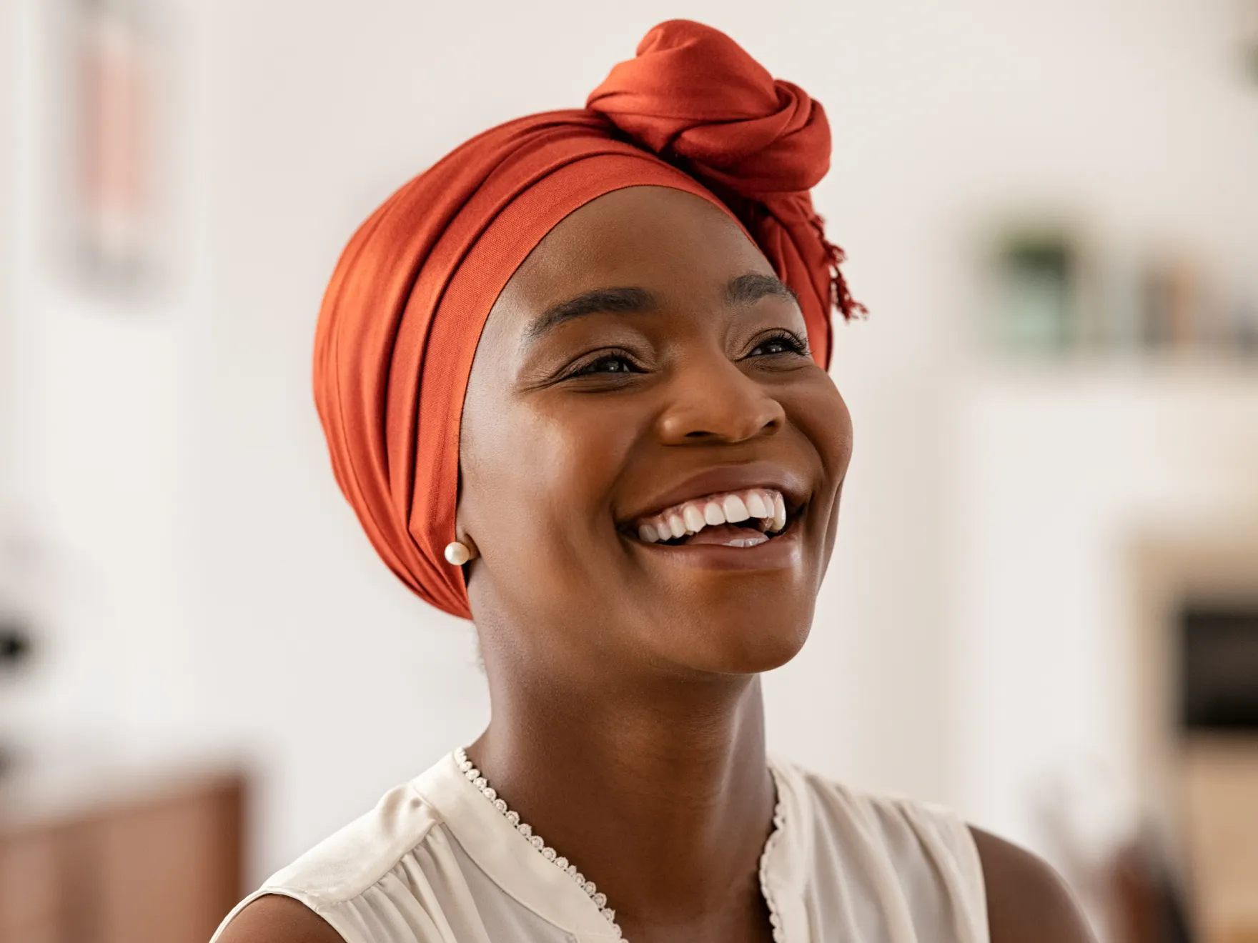 Woman smiling warmly at dental office, wearing red head wrap and pearl necklace