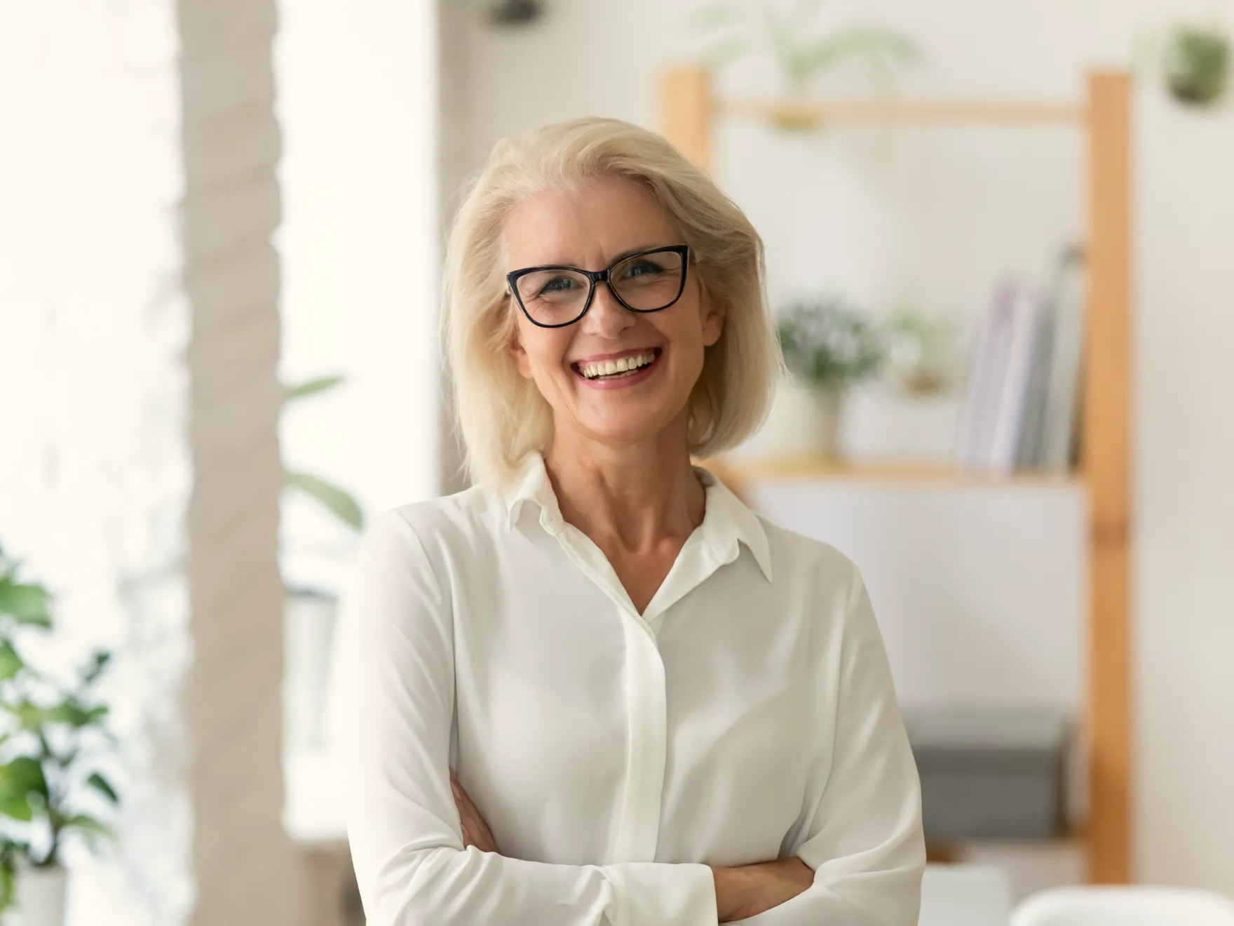 Smiling woman with blonde hair and glasses wearing white shirt in modern dental office interior.