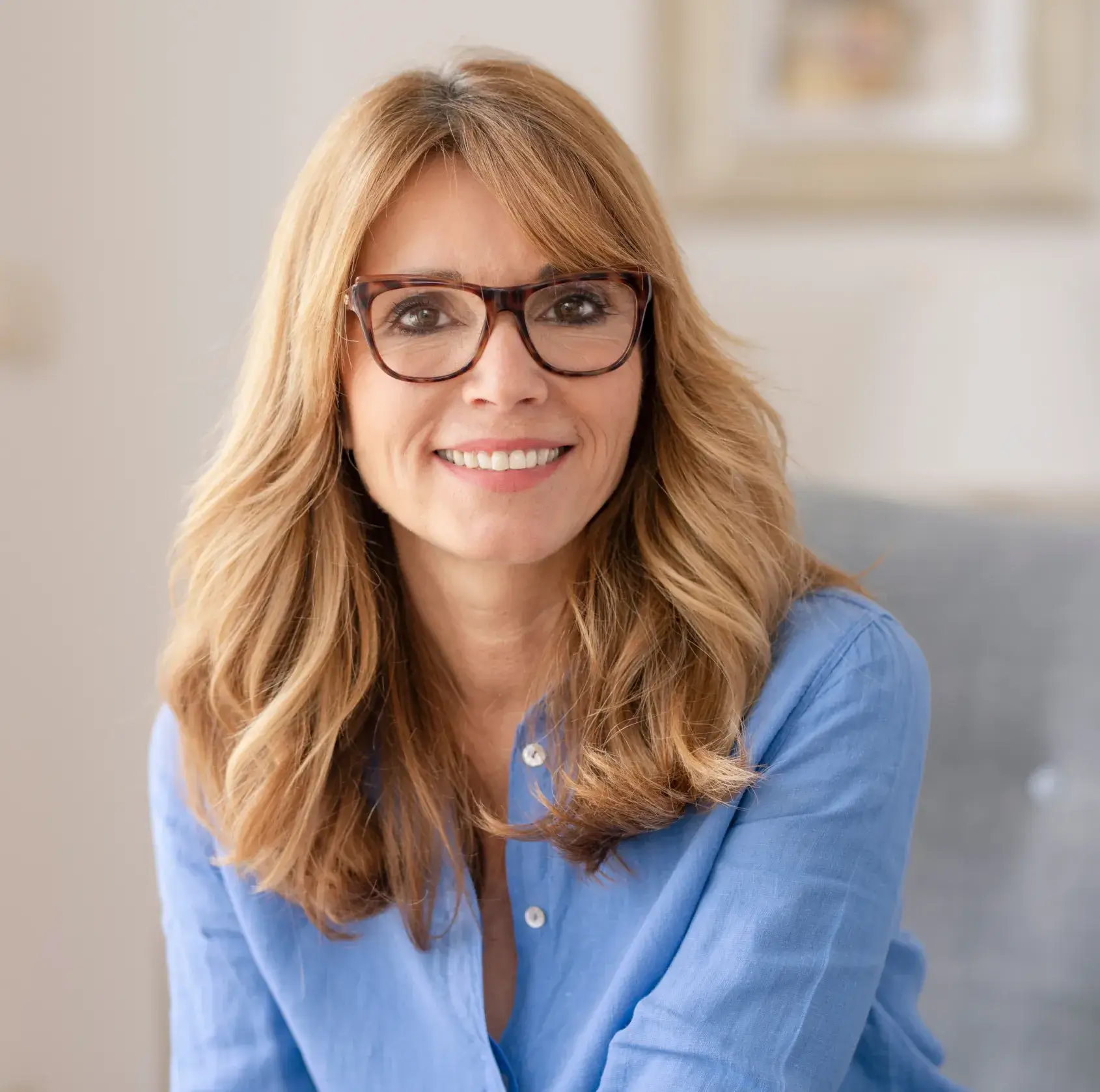 Professional woman with glasses smiling in dental office setting wearing blue shirt