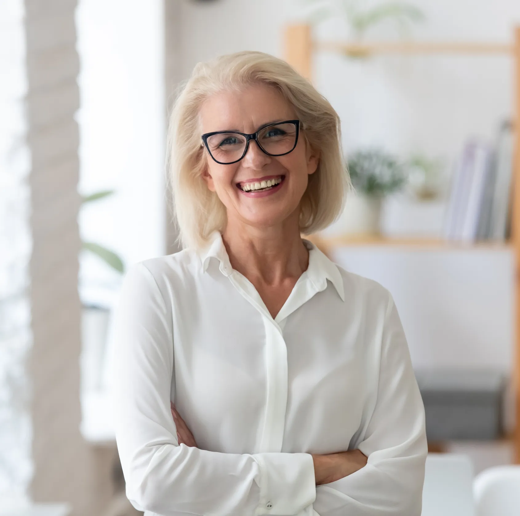 Professional woman in white shirt and glasses smiling in modern dental office setting.