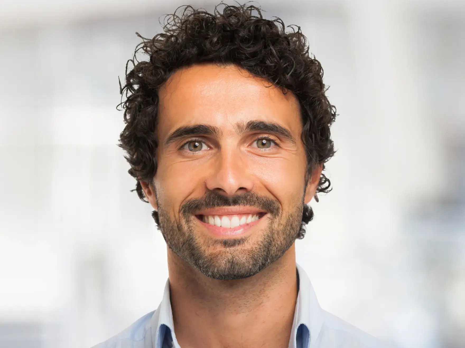 Professional headshot of smiling man in light blue shirt against blurred background.