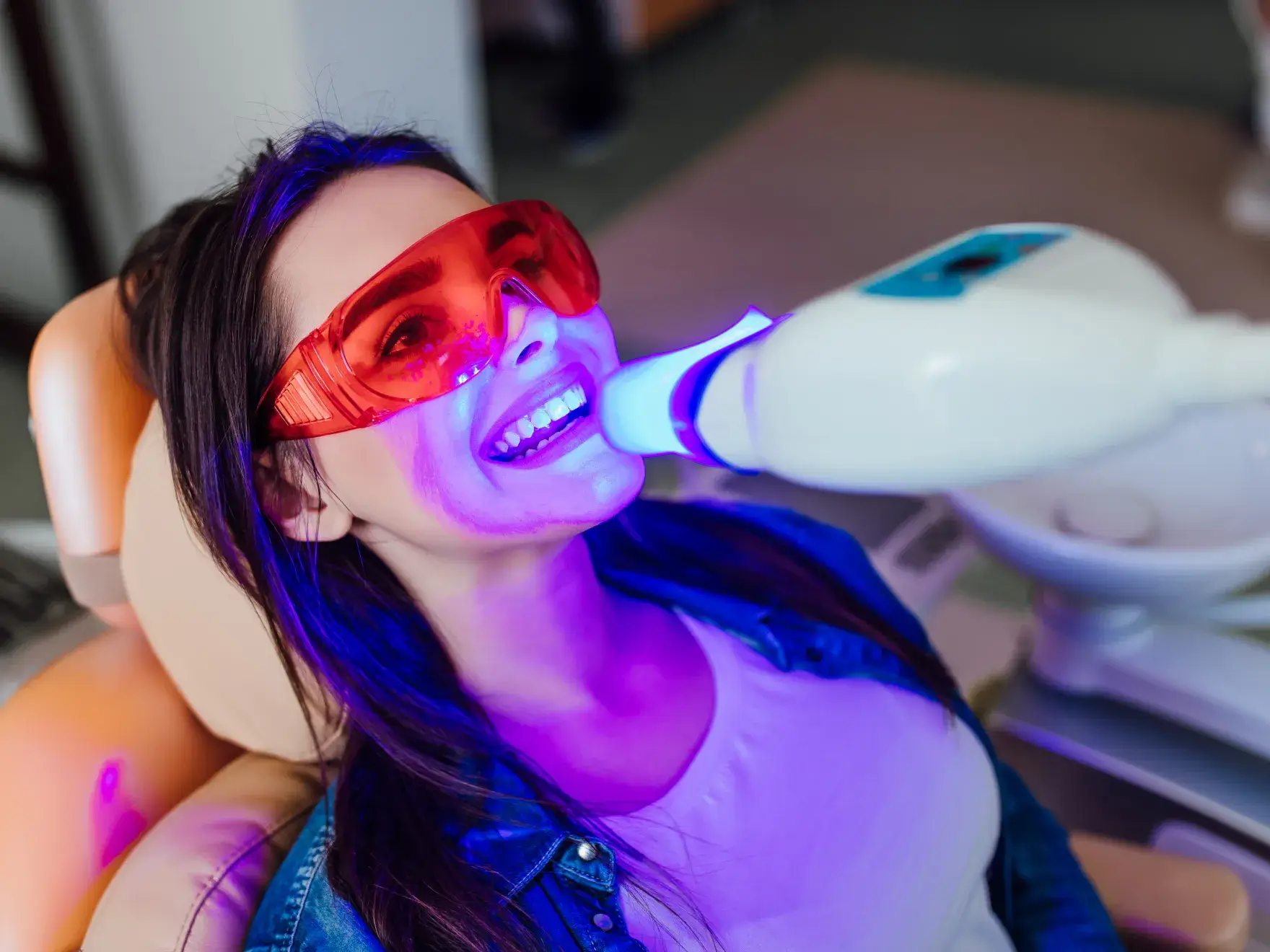 Patient receiving professional teeth whitening treatment with LED light device at dental clinic.