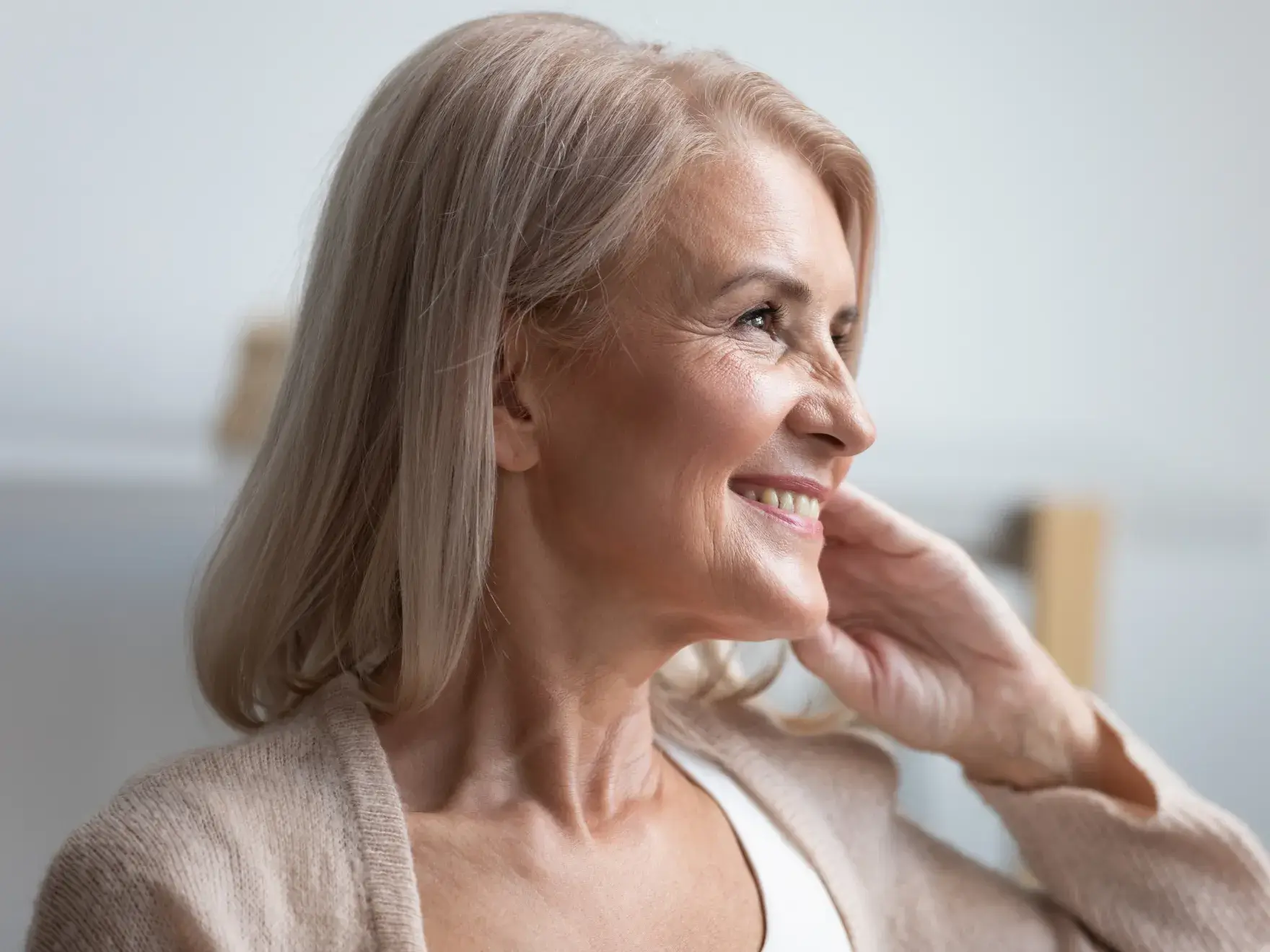 Mature woman smiling thoughtfully with hand to face in dental office setting.