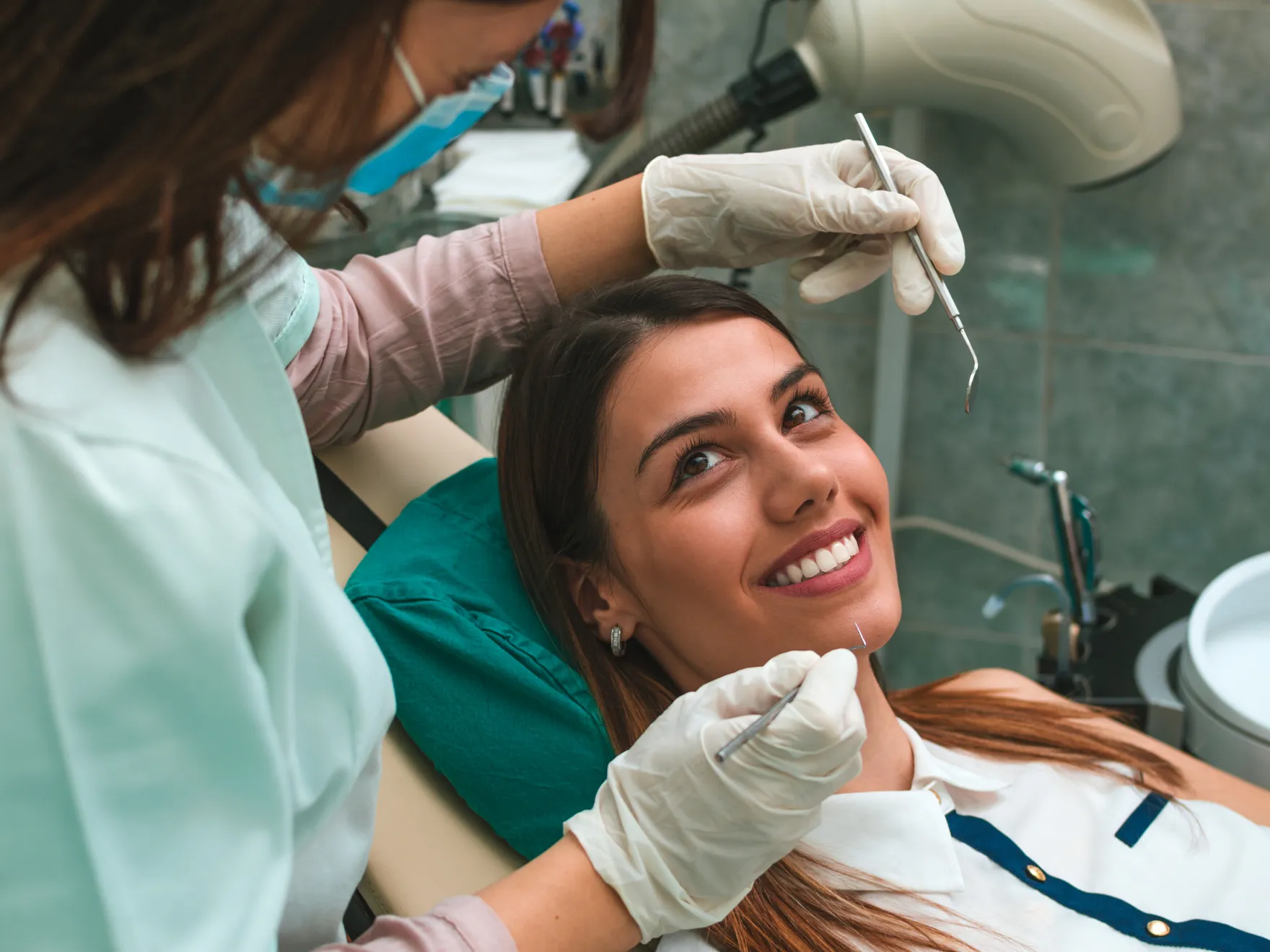 Dental hygienist examining patient's teeth with tools in modern dental office setting.