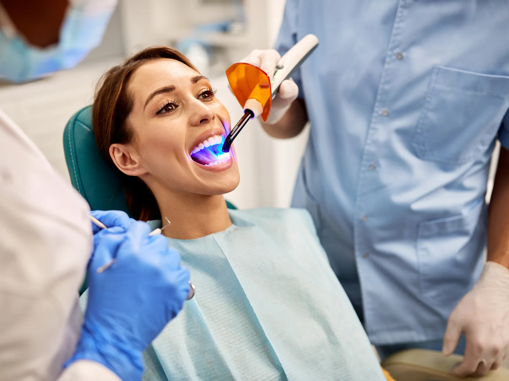Woman receiving dental treatment with UV curing light in dental office setting.