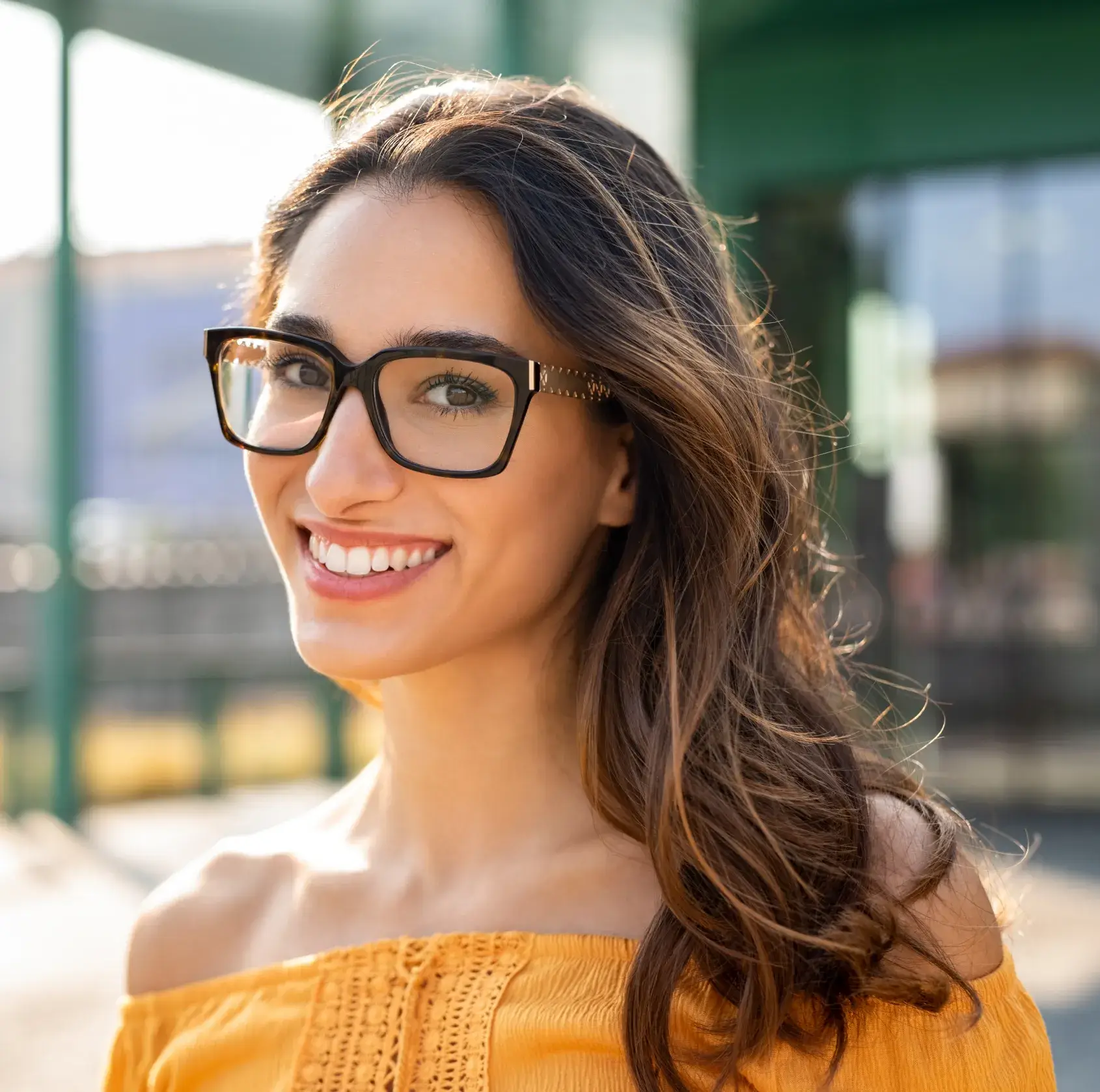 Smiling woman wearing glasses and yellow top at outdoor town center location.
