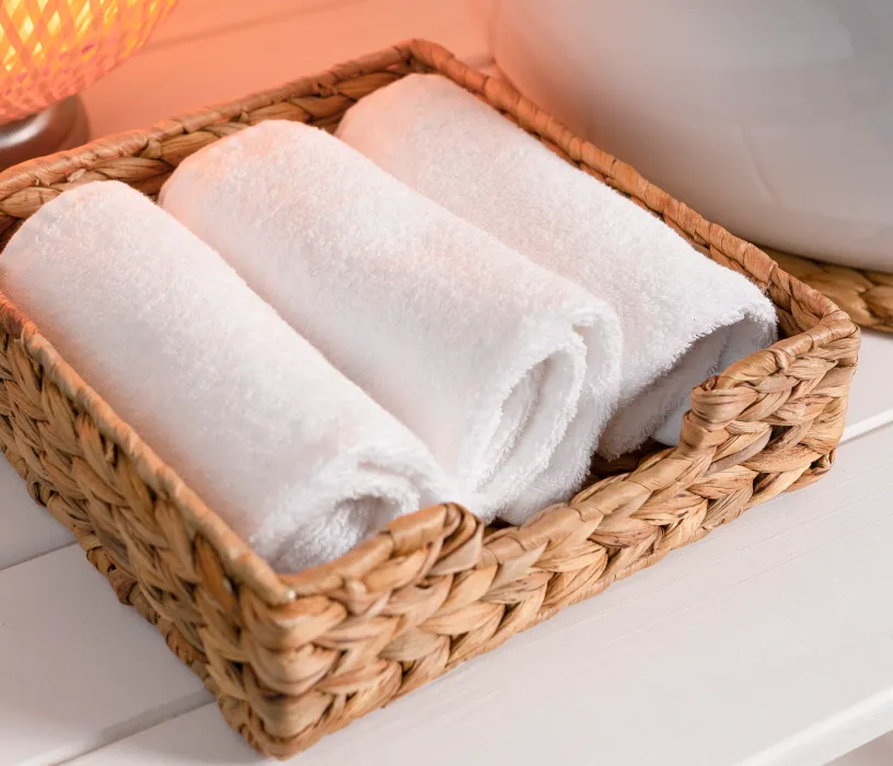 White rolled towels neatly arranged in a woven basket on a white shelf.