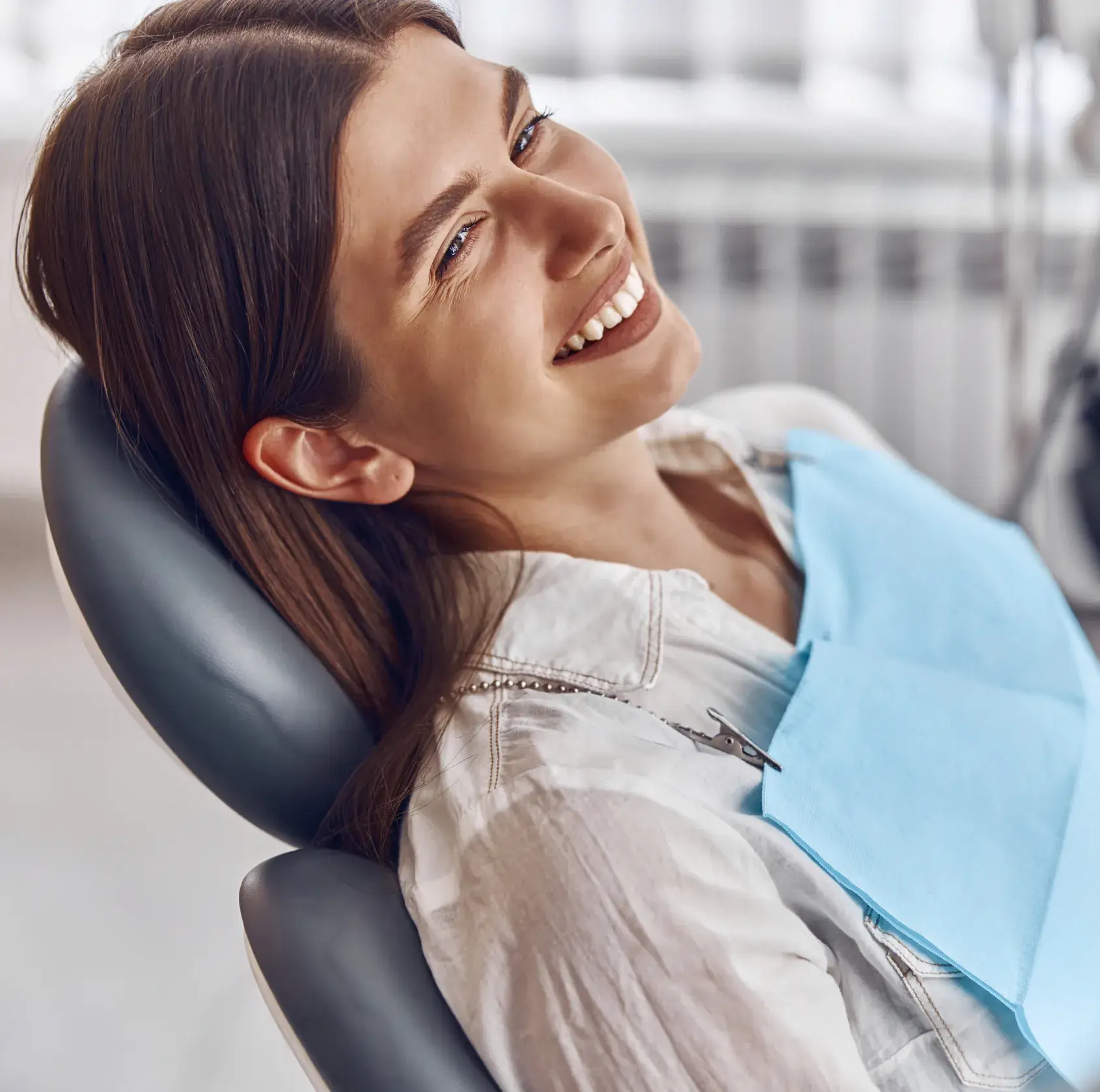 Smiling woman in dental chair wearing blue bib at modern dental office
