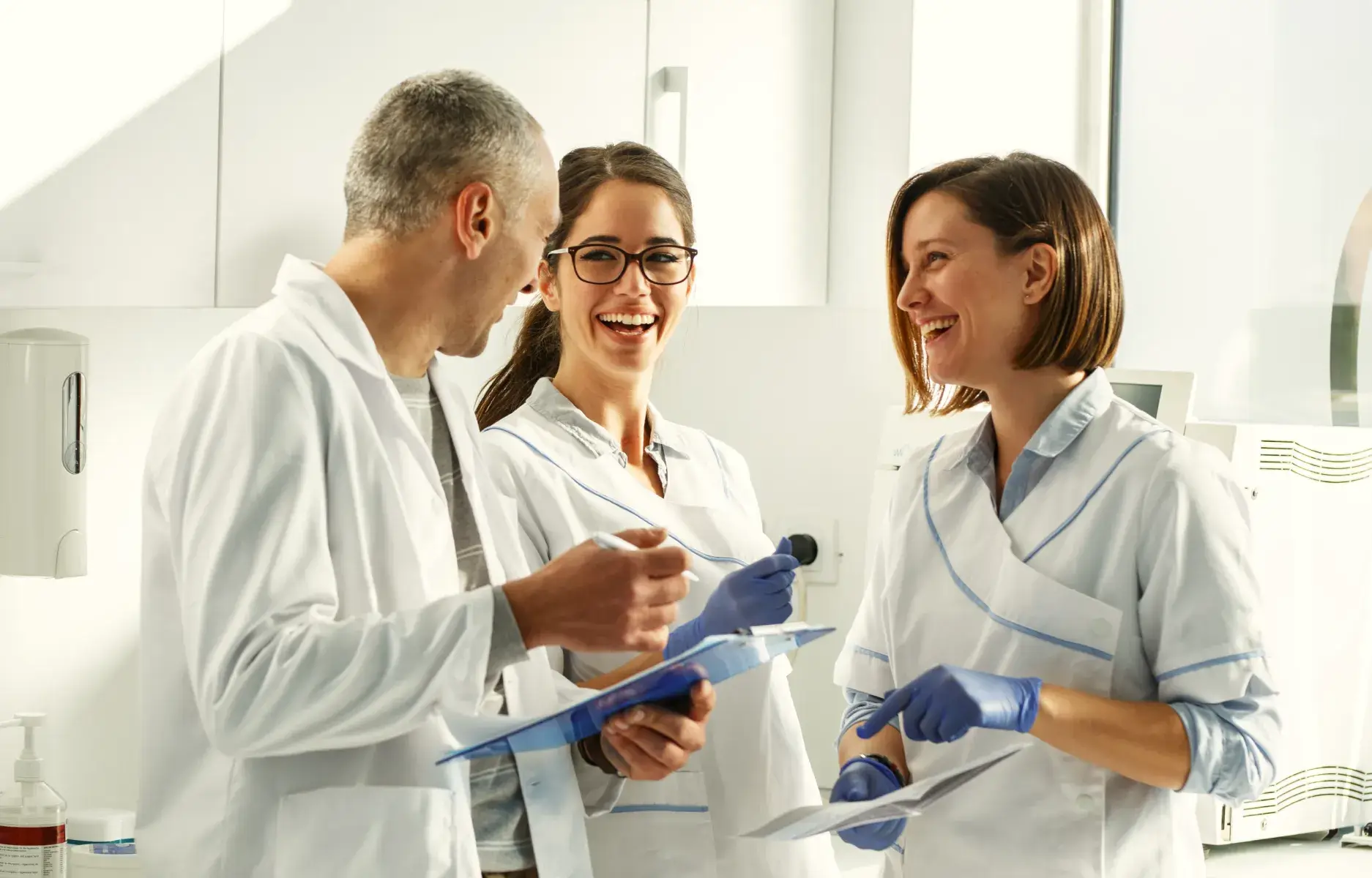 Three dental professionals in white coats discussing patient records in a modern clinic setting.