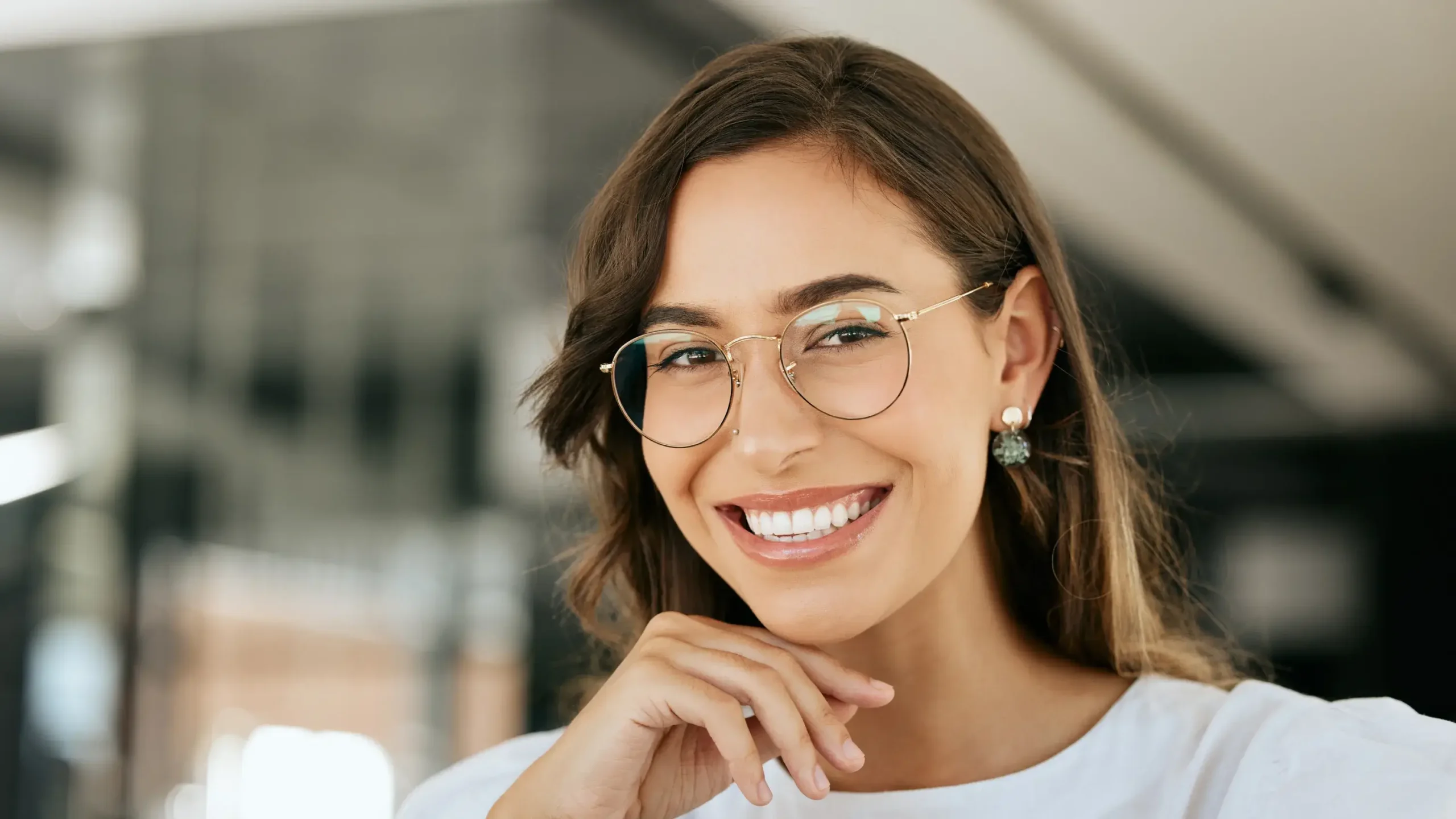 Smiling woman wearing glasses and pearl earrings in modern dental office setting.