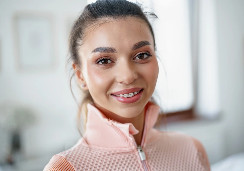 Young woman smiling at camera in bright dental office setting, wearing pink top.