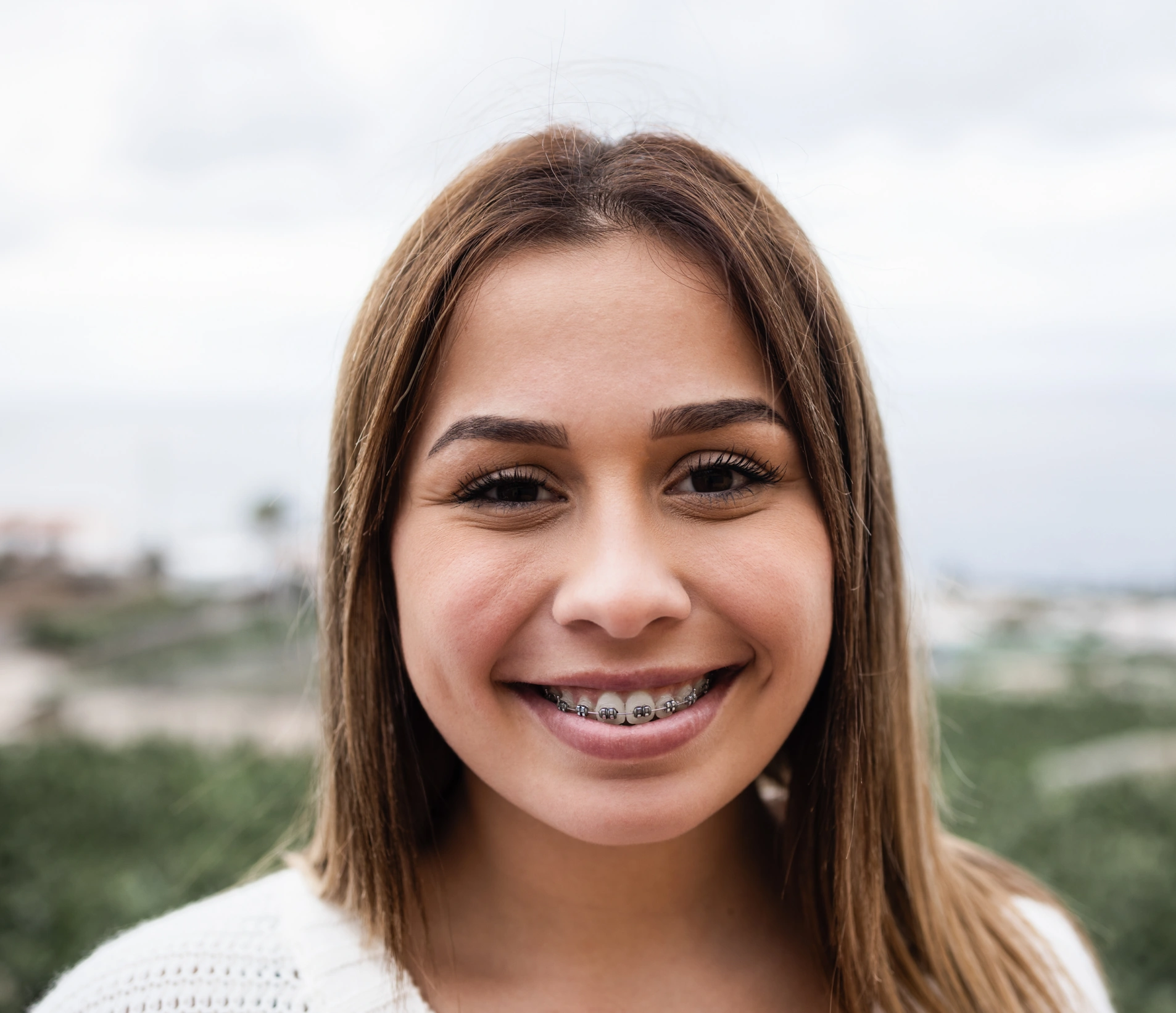 Young woman smiling at camera wearing dental braces, outdoor landscape background