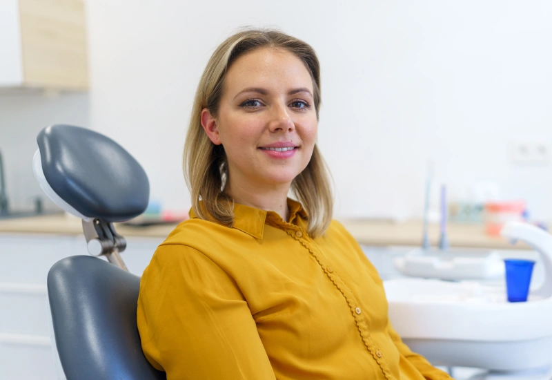 Professional woman in yellow shirt seated in dental office treatment room