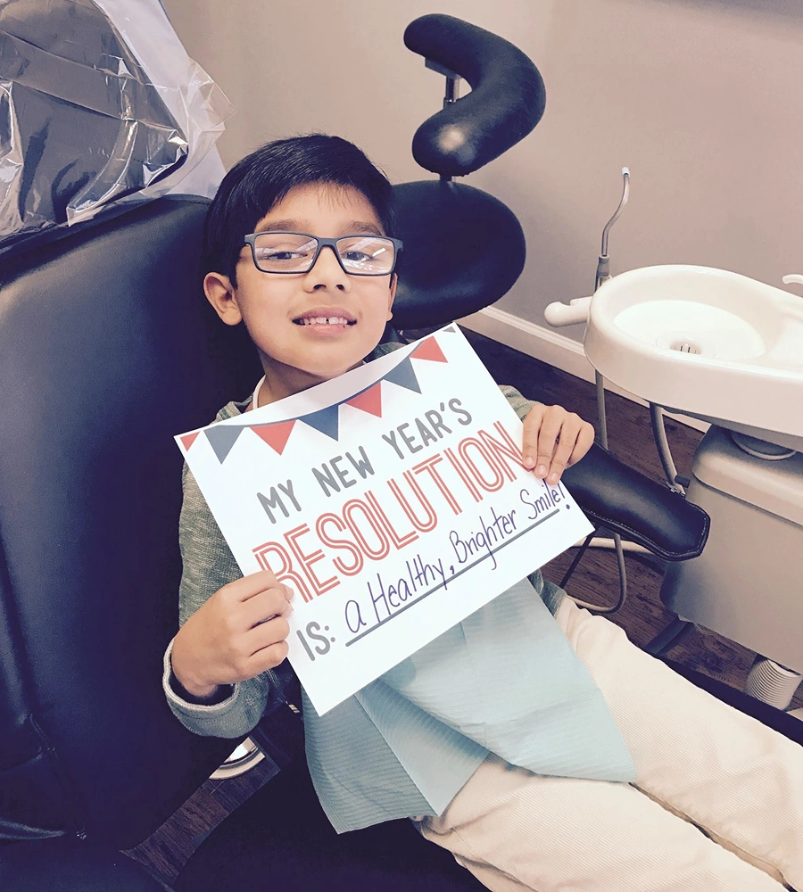 Young boy in dental chair holding New Year's resolution sign about healthy smile.