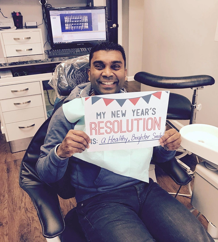 Man in dental office holding New Year's resolution sign about healthy smile.