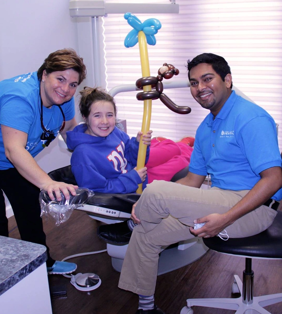 Pediatric dental team members with young patient holding balloon animal in dental office treatment room.