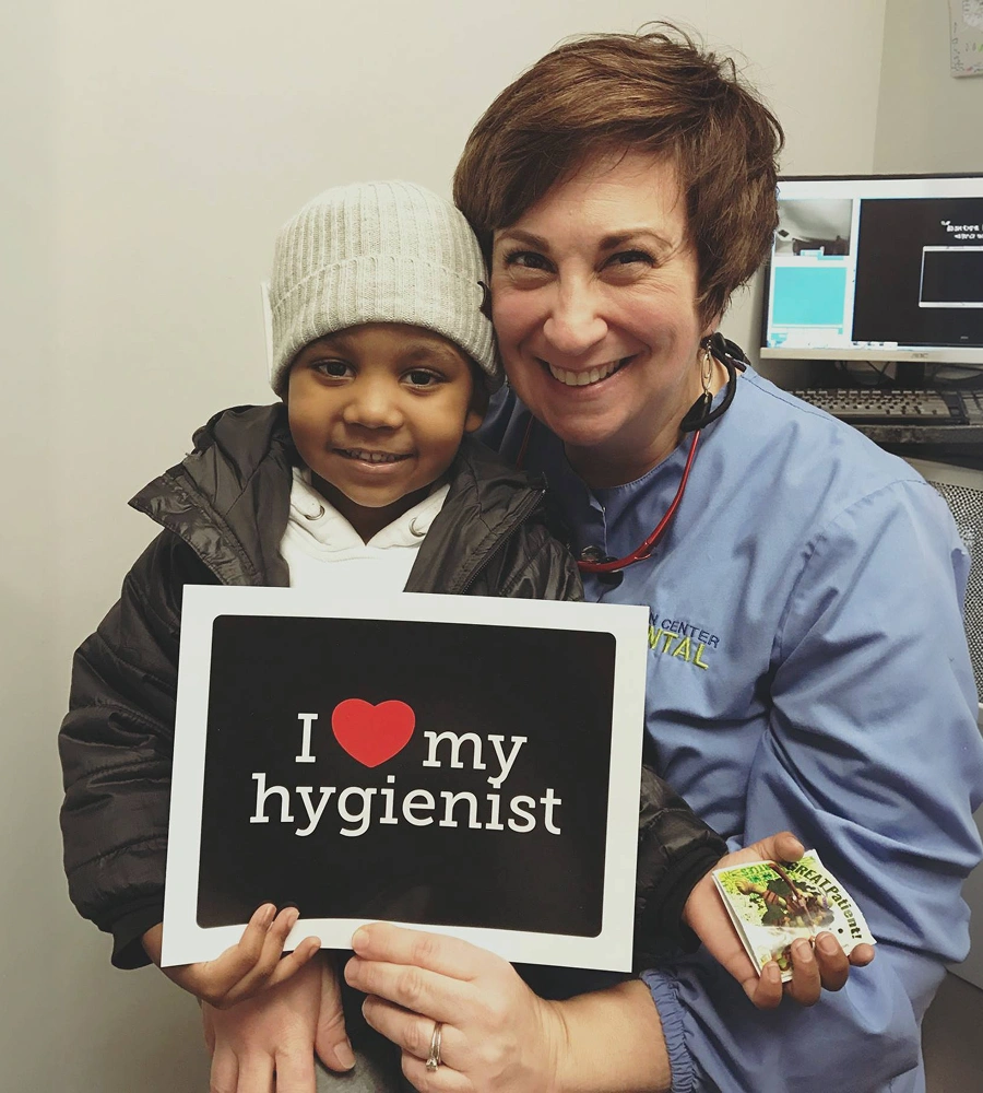 Dental hygienist and child hold sign reading "I love my hygienist" in dental office.
